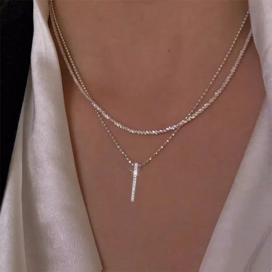 Layered silver chain necklaces with a vertical bar pendant worn on neck.