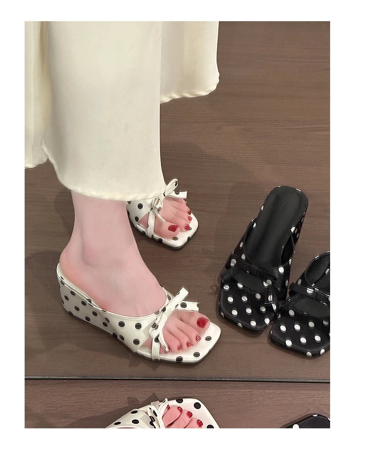White and black polka dot wedge sandals with bow straps, worn for casual daily outfits.