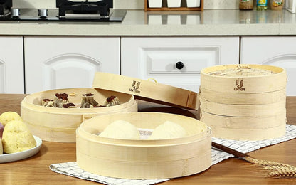 Round bamboo dumpling steamers with lids, holding bao buns and dumplings, on a kitchen table.