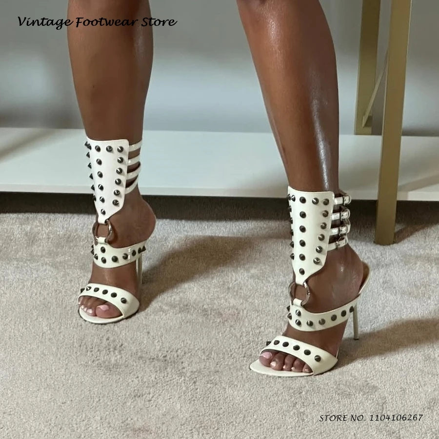 White strappy stiletto heels featuring metal rivets and buckle closures for evening wear.