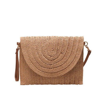 Tan straw woven crossbody bag with an envelope flap and adjustable strap for beach outings.