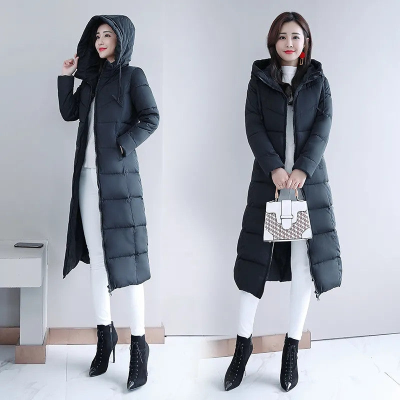 Woman wearing a black long hooded puffer parka jacket with horizontal quilting, over white pants and black boots.