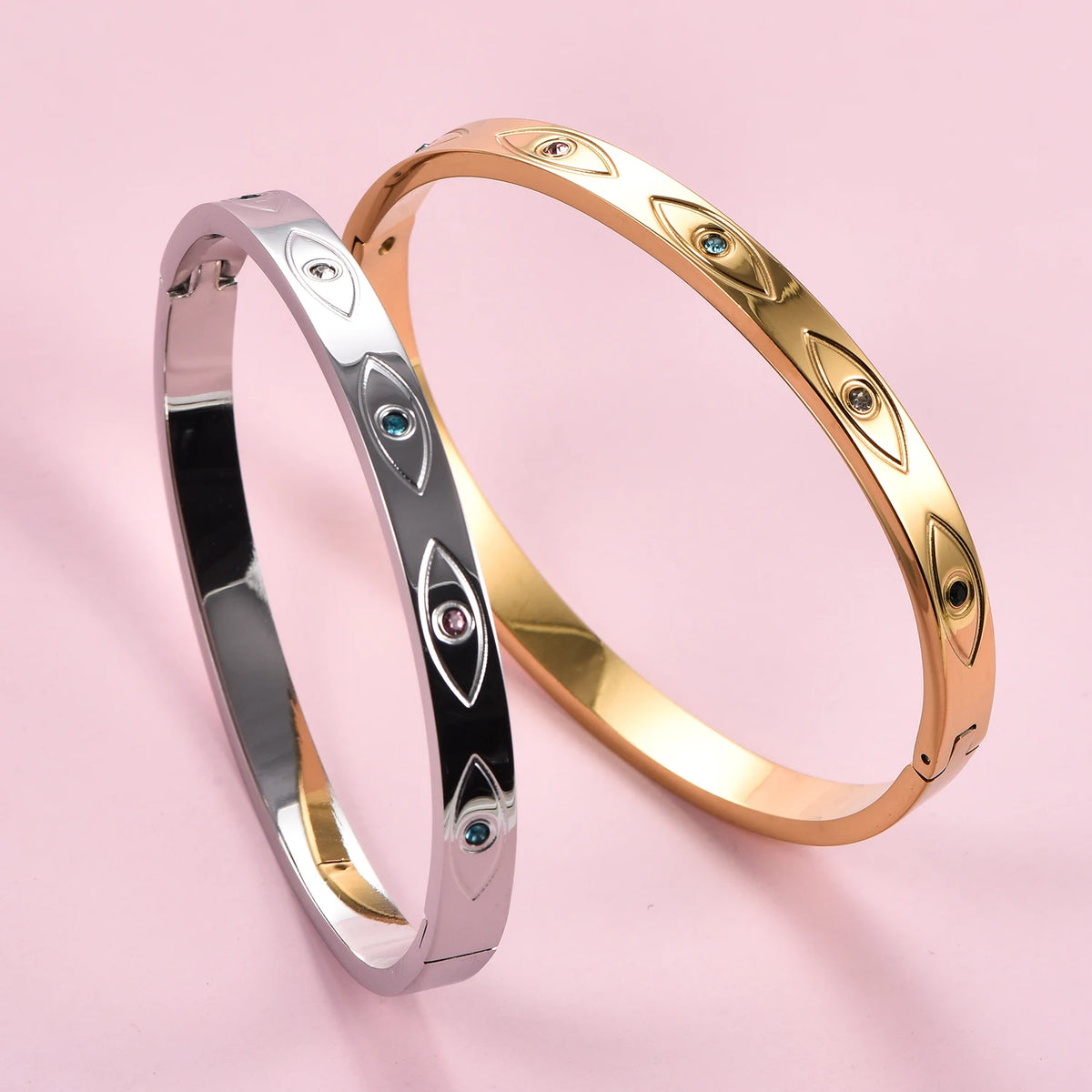 Silver and gold stainless steel cuff bangles with engraved evil eye motifs inset with small colored crystals.
