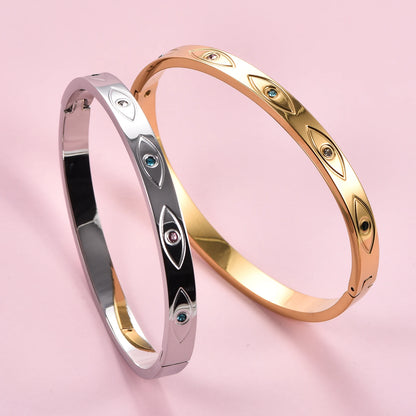 Silver and gold stainless steel cuff bangles with engraved evil eye motifs inset with small colored crystals.
