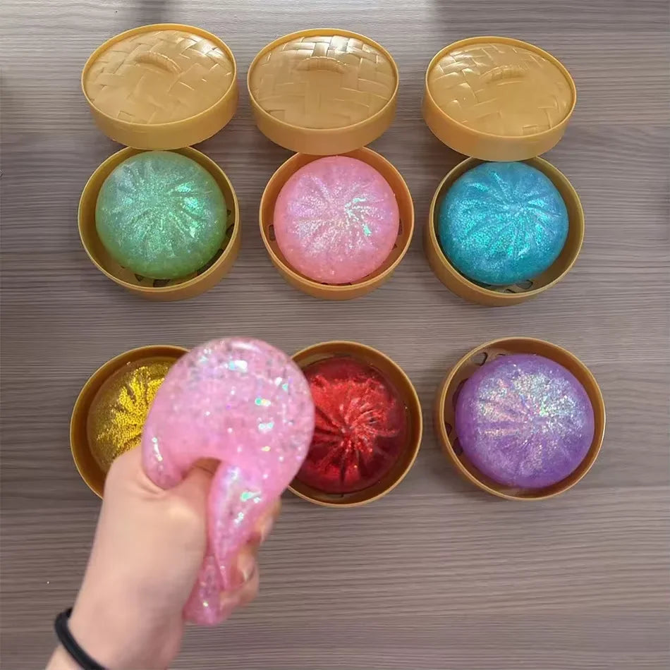 Glittery, stretchy dumpling squishy fidget toy in mini plastic steamer baskets for sensory play and stress relief.