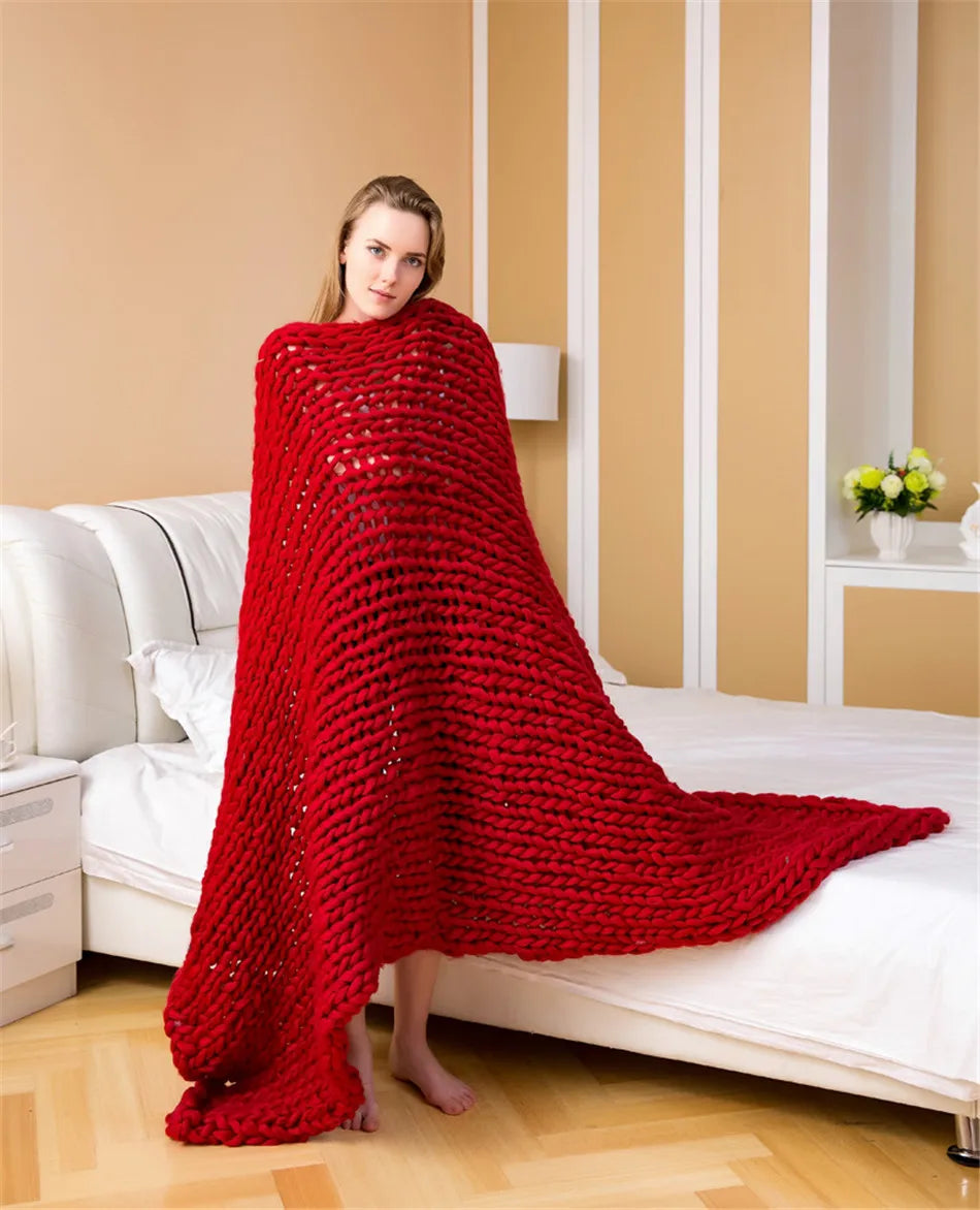 Red chunky knit yarn blanket draped over a standing woman in a bedroom.