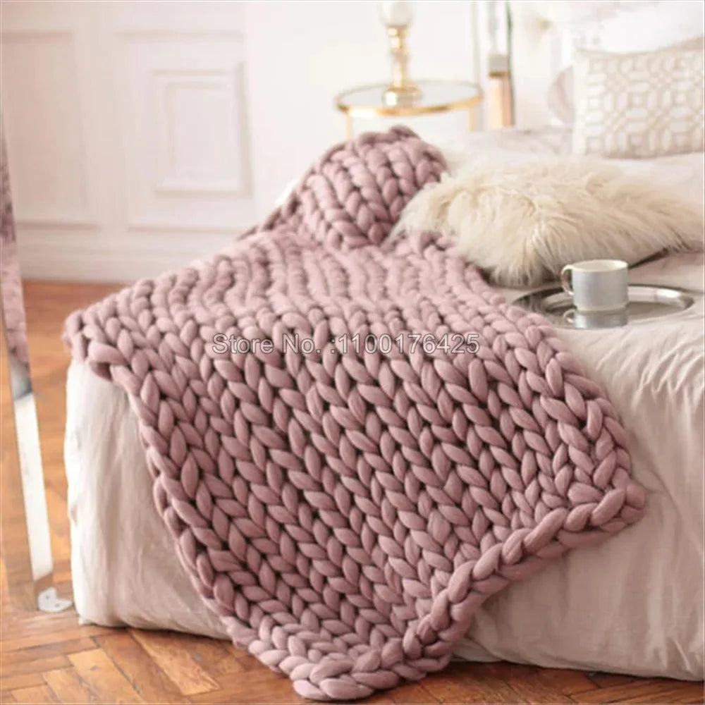 Chunky knit blanket in dusty pink yarn, draped over a bed.