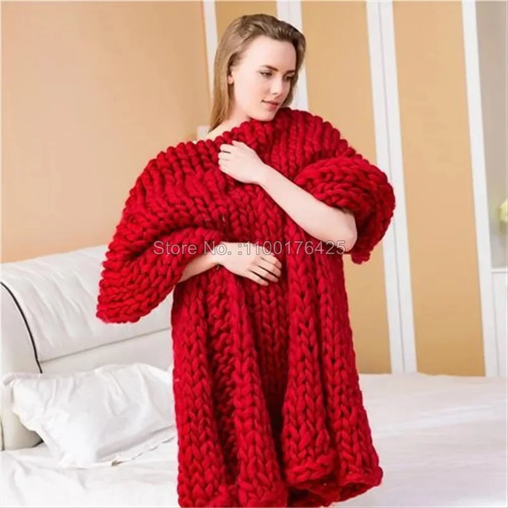 A woman wrapped in a thick, red chunky knit yarn blanket indoors.