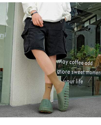 Olive green, slip-on sandals with thick platform soles and side vents worn with socks for all-day comfort.