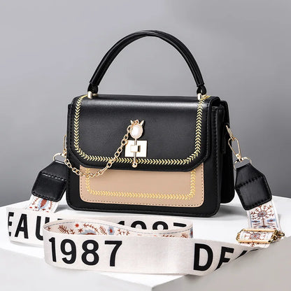 Black and beige faux leather handbag with gold hardware, a top handle, and a patterned crossbody strap.