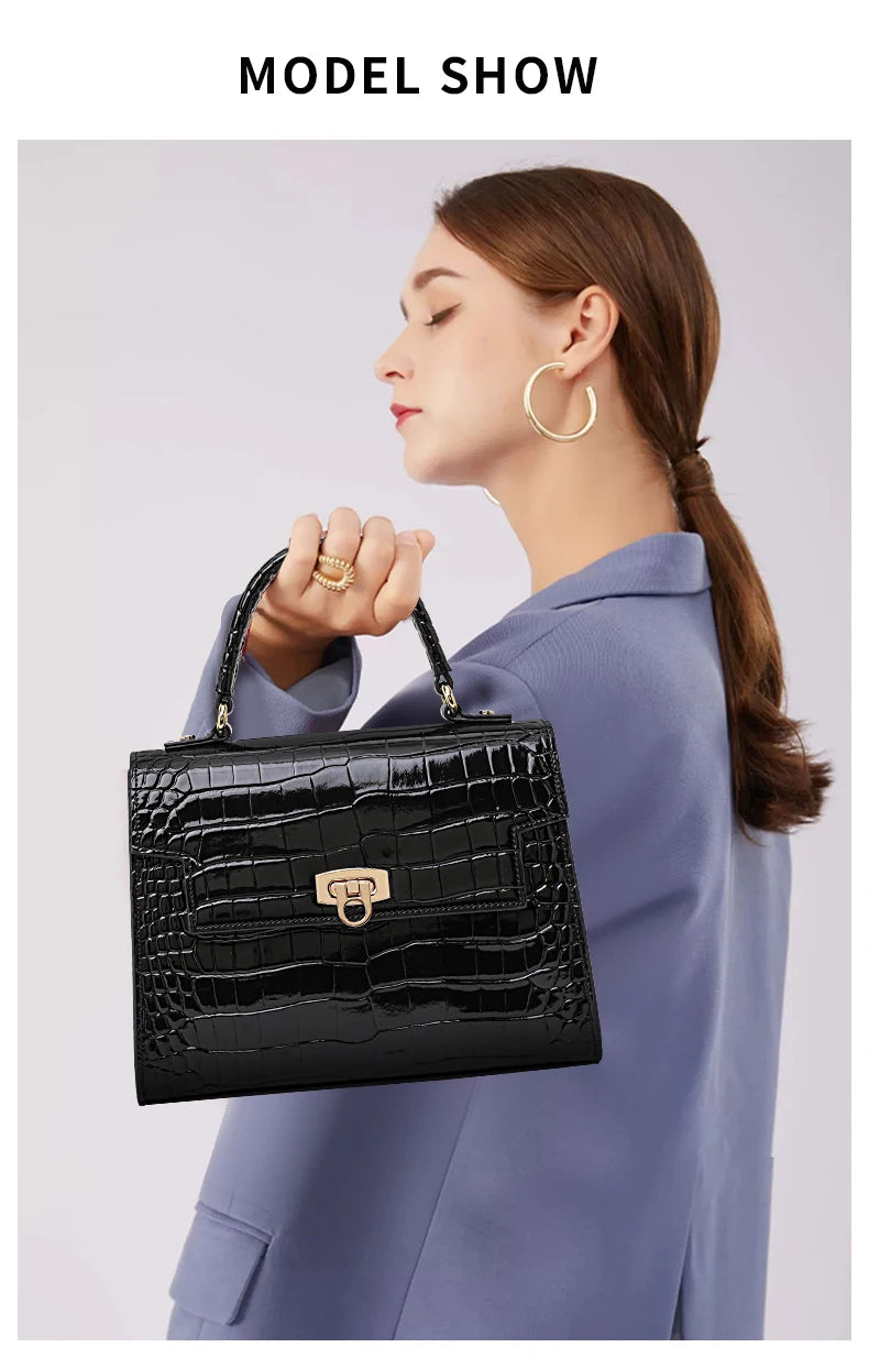 A black patent leather handbag with a crocodile pattern, top handle, and a gold clasp, held by a woman.