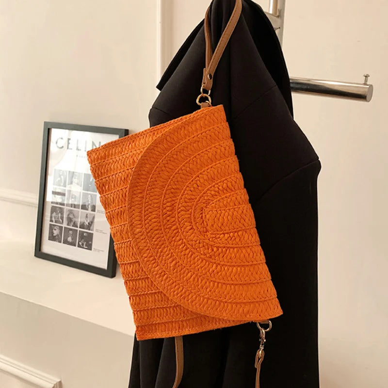 Bright orange woven straw envelope crossbody bag with an adjustable strap for beach outings.