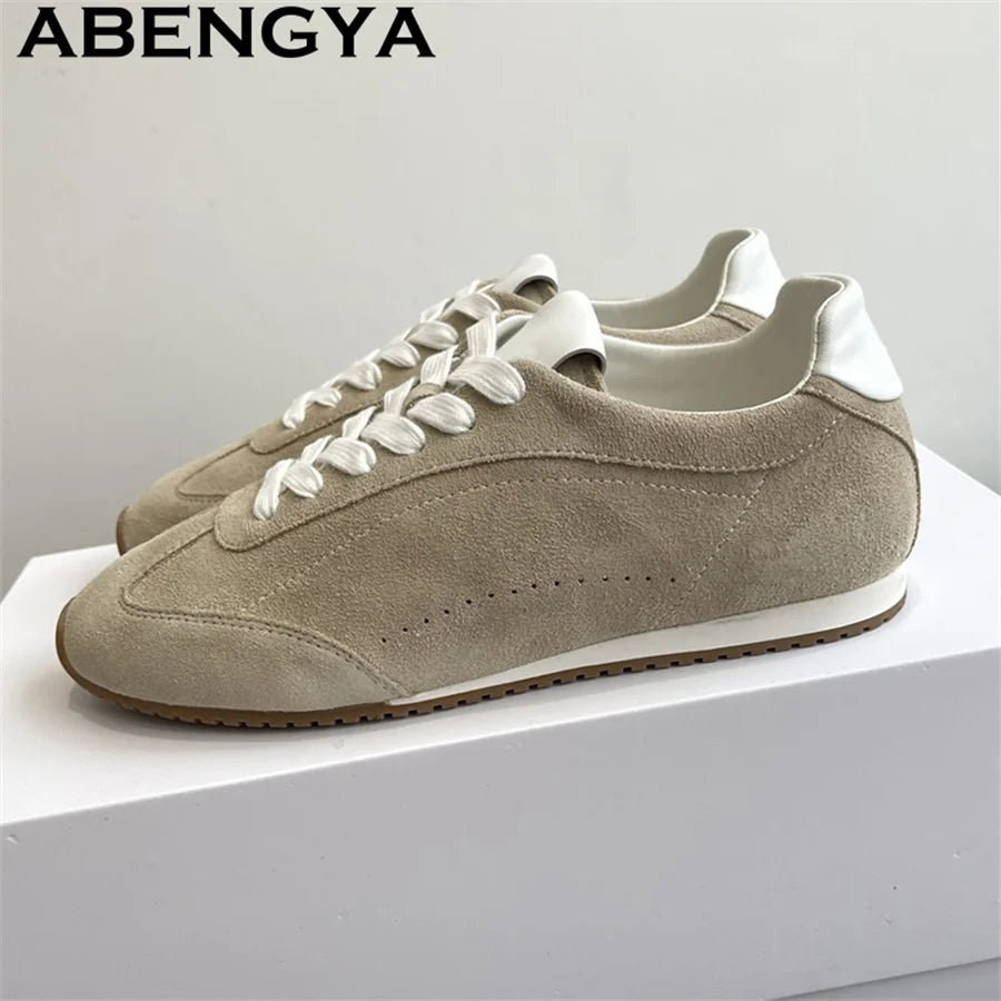 Beige suede lace-up sneakers with white laces, white heel tabs, a white midsole, and a ridged brown rubber sole.