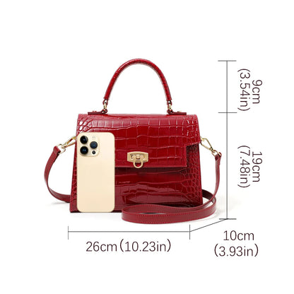 Red patent leather crocodile-pattern handbag with a top handle, turn-lock closure, and detachable crossbody strap.