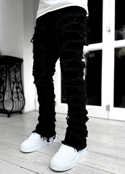 Black distressed denim jeans with frayed patchwork details and a fitted silhouette for casual everyday wear.