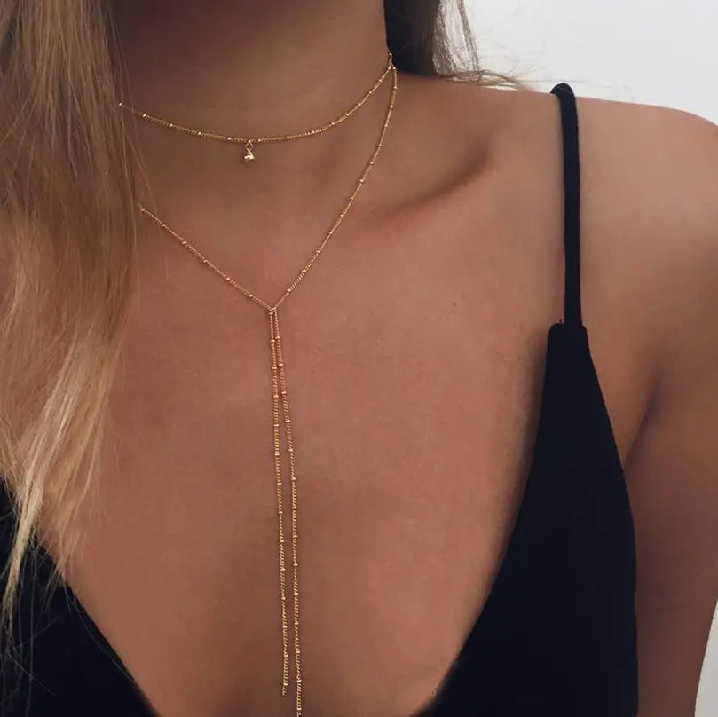 Gold multilayer lariat necklace with bead-accented chains and a small pendant worn on a person.