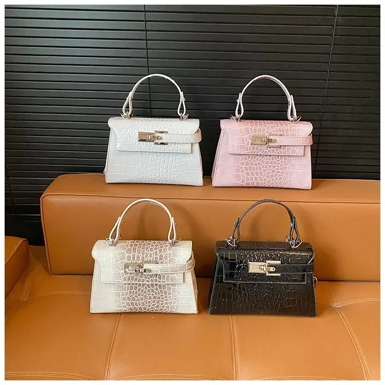 Four faux leather satchel diaper bags with structured crocodile textures and silver zip closures for carrying baby items.
