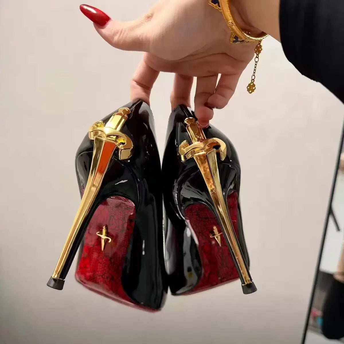 Black faux leather pointed toe stiletto pumps with gold sword heels and red patterned soles for formal evening events.