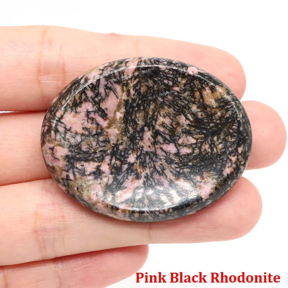 Smooth oval pink and black rhodonite home decor palm stone held in a hand for meditation.