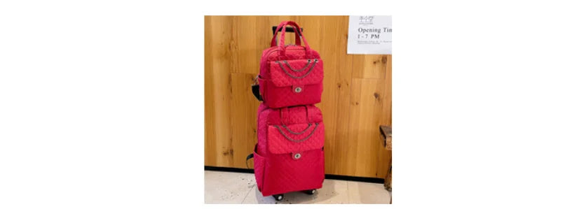 Hot pink quilted rolling luggage set with chain accents and dual compartments against a wood-paneled wall.