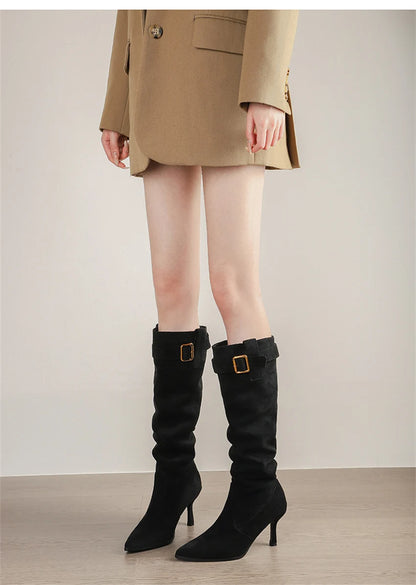 Black suede pointed-toe knee-high boots with thin high heels and a gold-buckled strap.