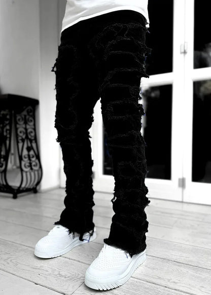 Black distressed denim with heavy ripped detailing in a slim straight fit, suitable for casual streetwear outfits.