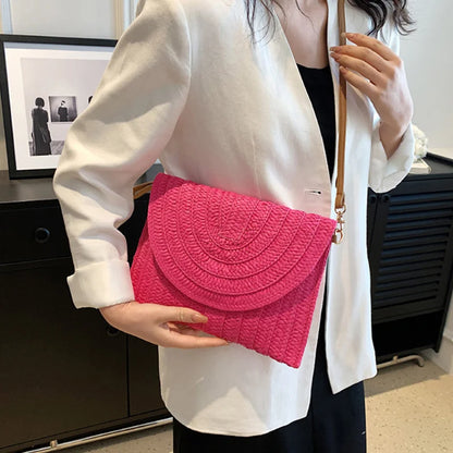 Hot pink straw woven envelope crossbody bag with an adjustable strap for beach outings.