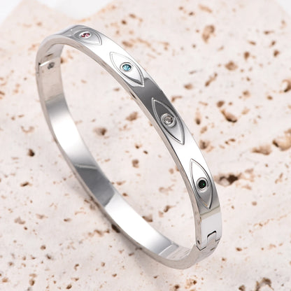 Silver stainless steel cuff bangle with engraved evil eye motifs inset with colorful crystals.