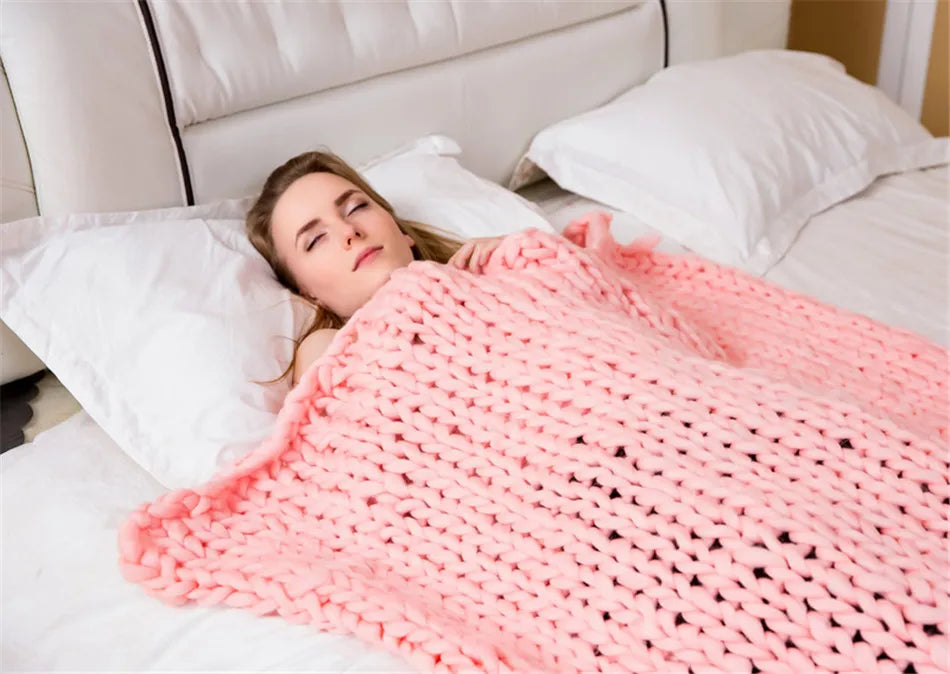 A woman sleeping on a bed under a thick, chunky knit pink yarn throw blanket.