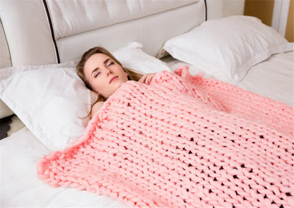 A woman sleeping on a bed under a thick, chunky knit pink yarn throw blanket.