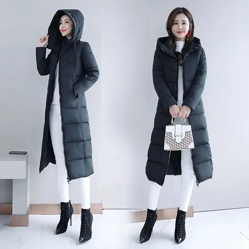 A woman modeling a black long puffer coat with a hooded, quilted design and front zipper closure.