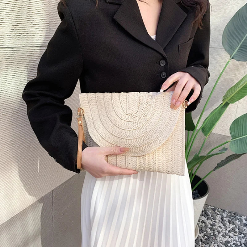 Beige straw envelope crossbody bag with a textured finish, carried as a clutch for beach outings.