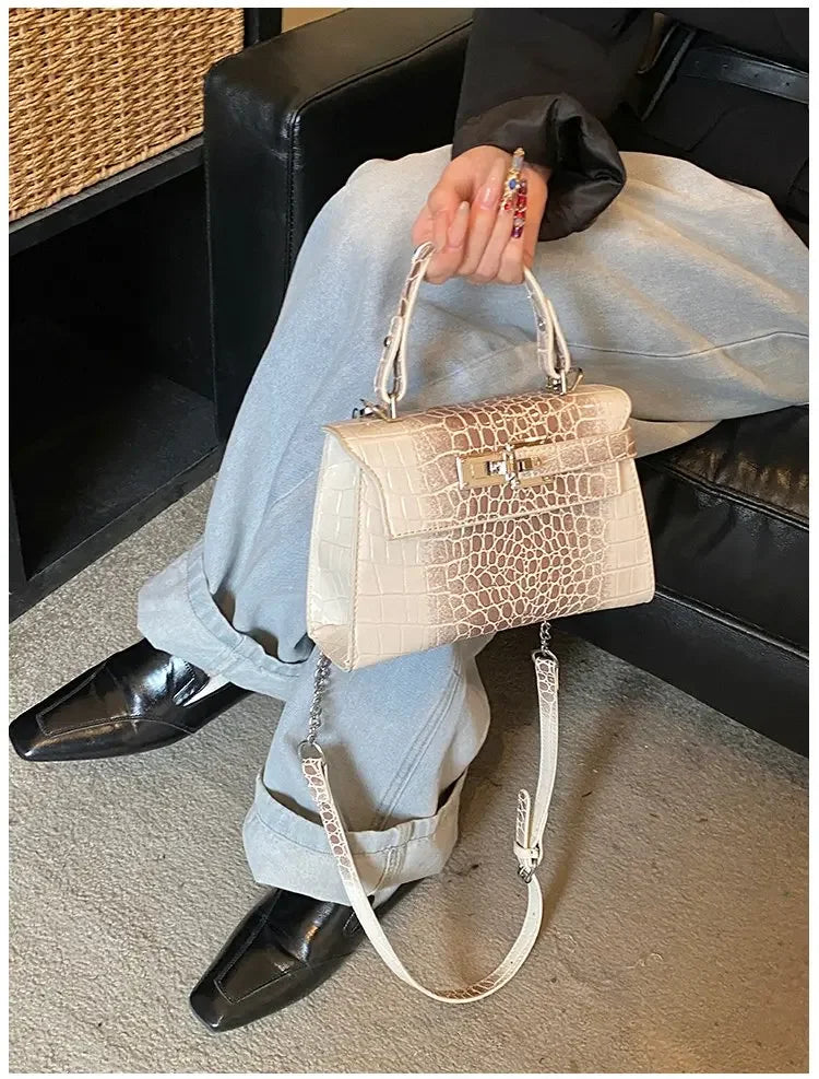 Beige faux leather crossbody diaper bag with croc-embossed texture, top handle, and adjustable strap for carrying items.