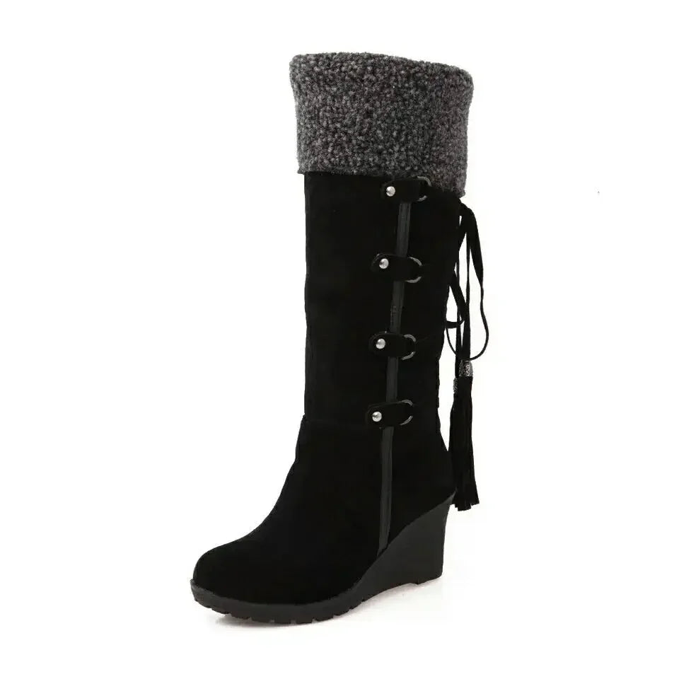 Black suede knee-high wedge snow boot with grey faux fur cuff, side straps, and tassels.