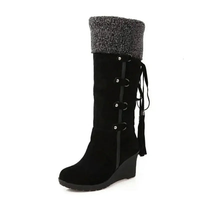 Black suede knee-high wedge snow boot with grey faux fur cuff, side straps, and tassels.