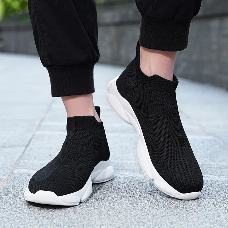 Black slip-on sneakers with breathable knit fabric and thick white platform soles for casual everyday wear.