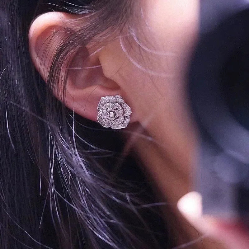 Silver-tone zircon stud earrings shaped like a hollow, layered camellia flower worn on an earlobe.
