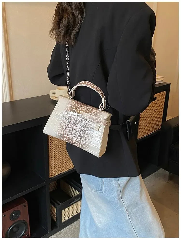 Beige faux leather crocodile-textured satchel with a metal chain strap for carrying baby essentials.