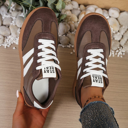 Brown suede and leather slip-on sneakers with white stripes and laces, worn for casual daily activities.