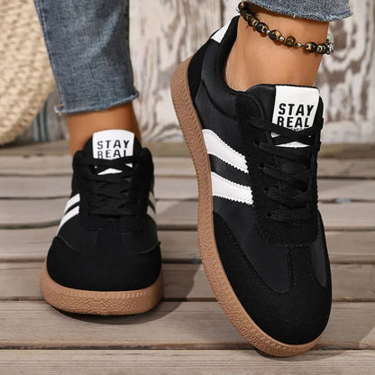 Black and white leather slip-on sneakers with gum soles and "Stay Real" tongue labels for casual daily wear.