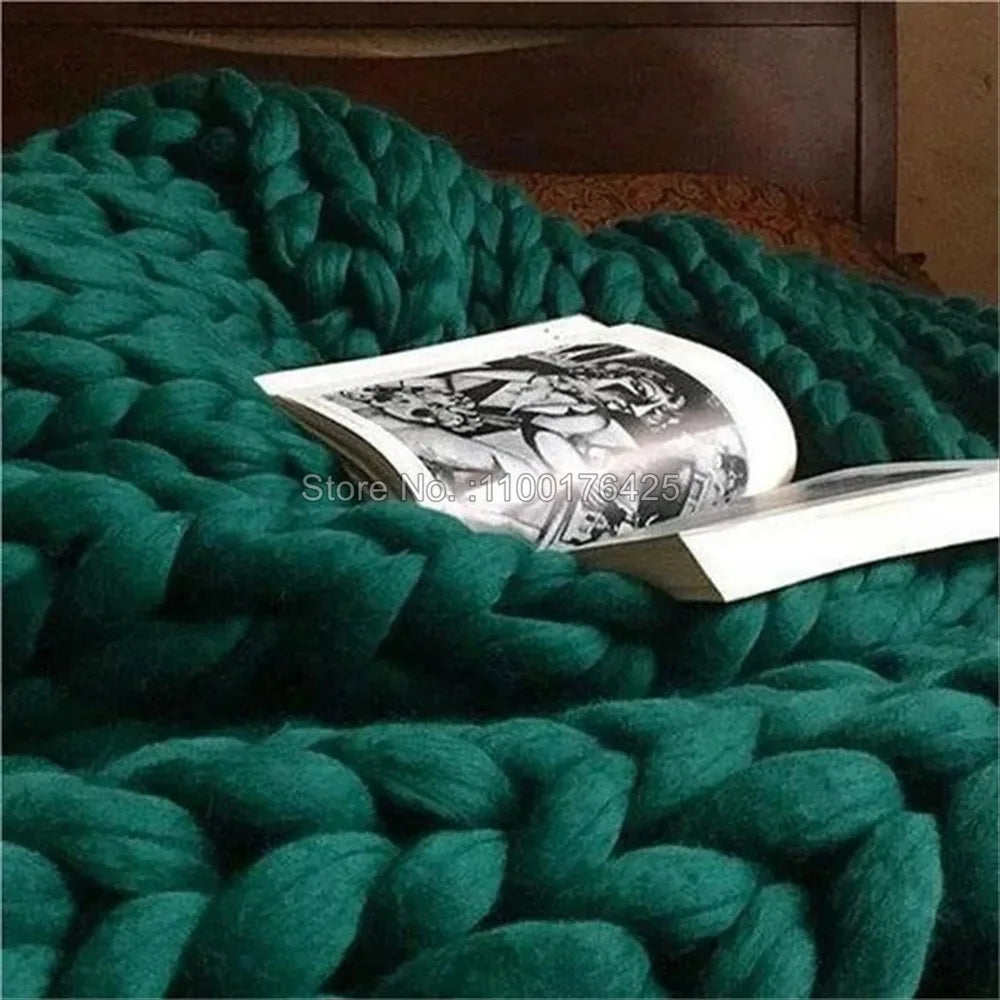 Dark green chunky hand-knitted yarn throw blanket draped on a bed with an open book.