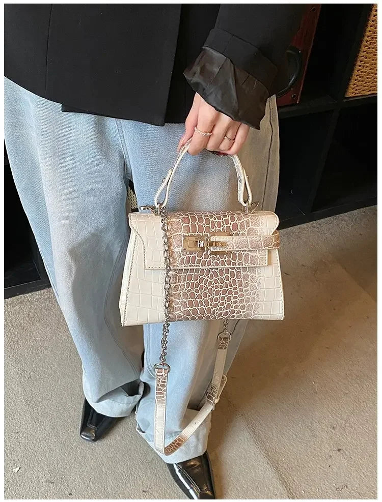 Off-white faux leather crossbody diaper bag with croc texture, gold hardware, and adjustable strap for parents on the go.