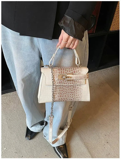 Off-white faux leather crossbody diaper bag with croc texture, gold hardware, and adjustable strap for parents on the go.