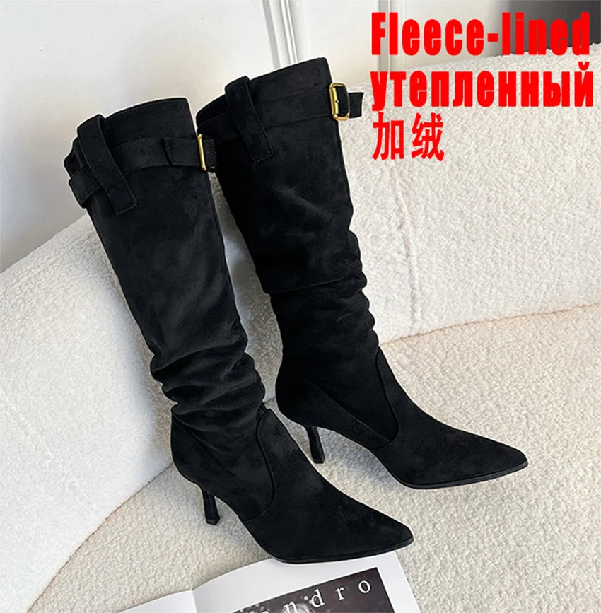 Black faux-suede knee-high boots with pointed toes, thin heels, slouchy shafts, and ankle buckle straps.