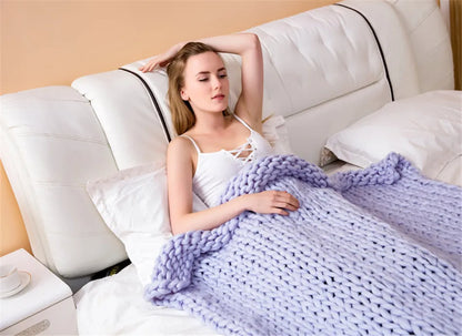 Light grey chunky knit throw blanket made of thick yarn, draped over a bed.
