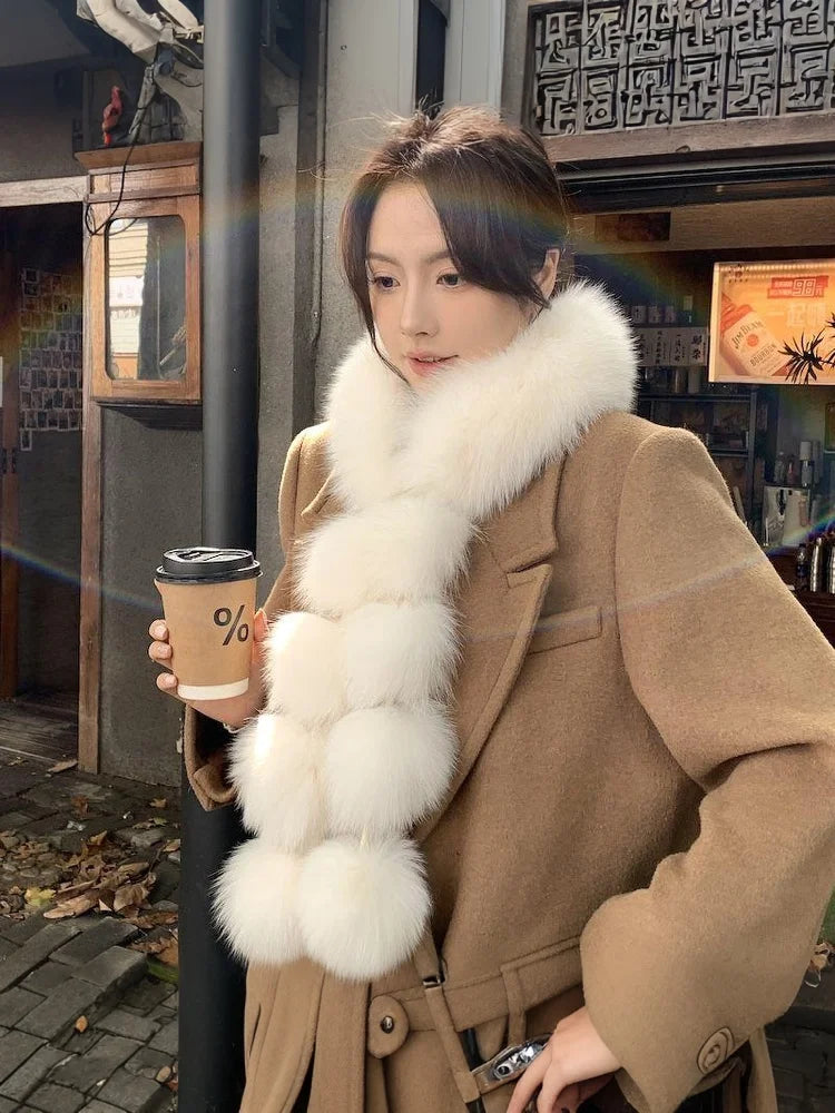 A woman wearing a white faux fox fur pom-pom scarf with a brown coat.