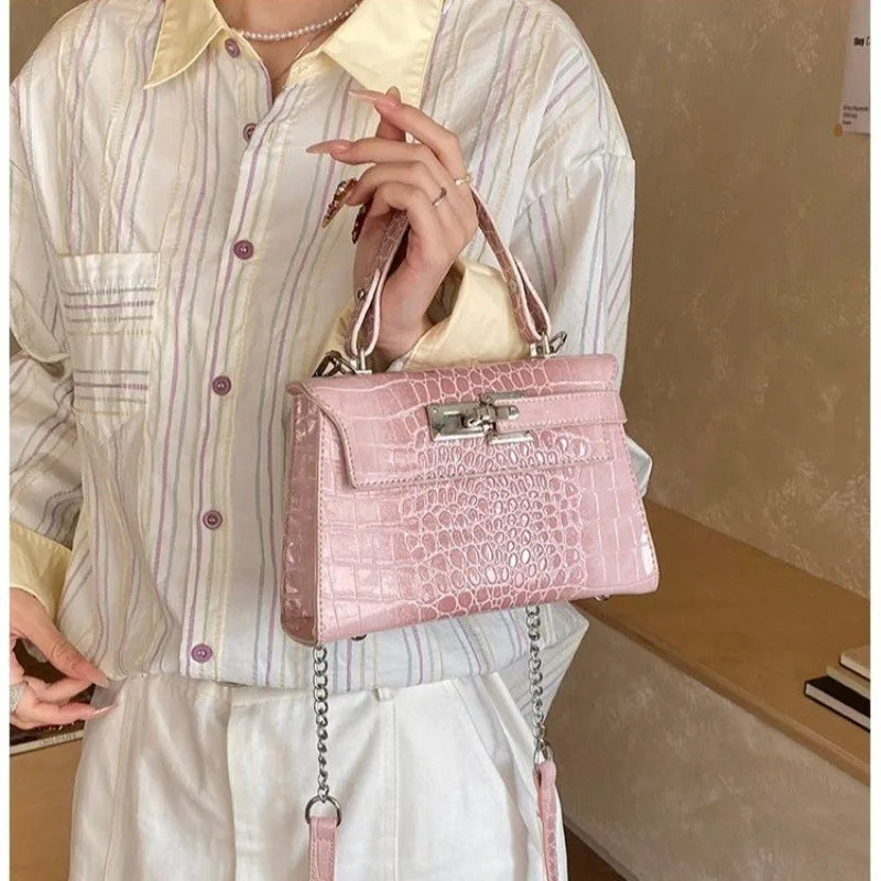 Pink faux leather diaper bag with a crocodile pattern, metal clasp, and multi-pocket design for organized baby gear.
