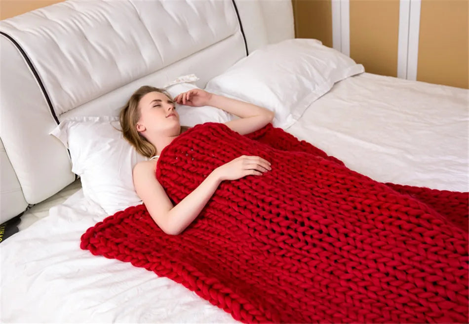 A woman lies in bed under a chunky, thick, red knit yarn throw blanket.