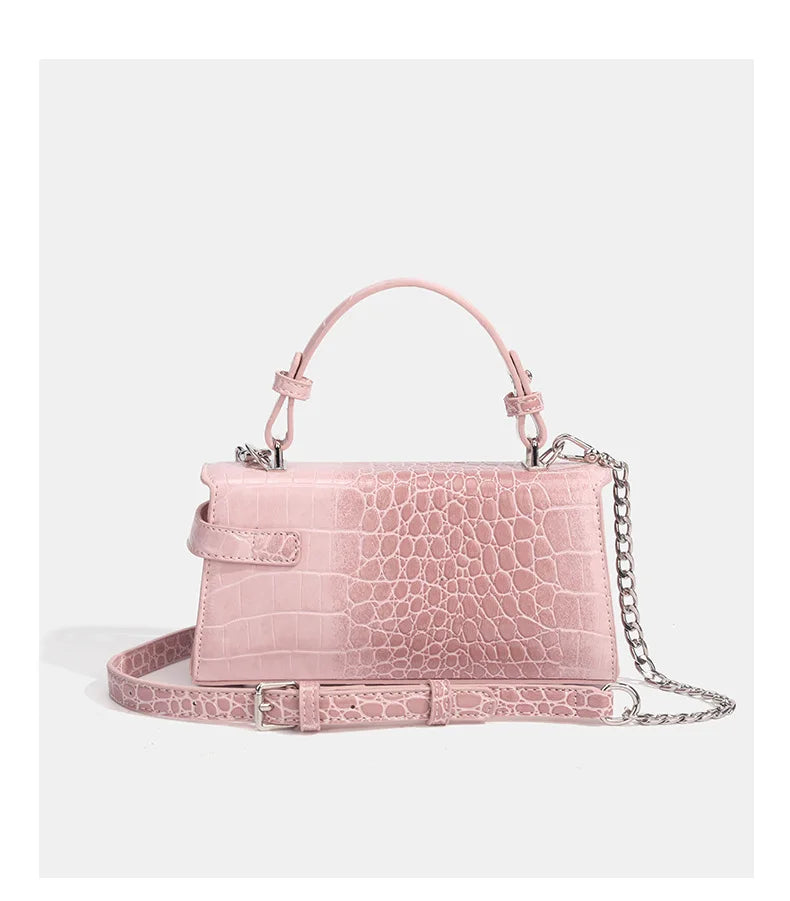Light pink faux leather crossbody bag with croc-embossed texture, silver chain strap, and adjustable buckle for travel.