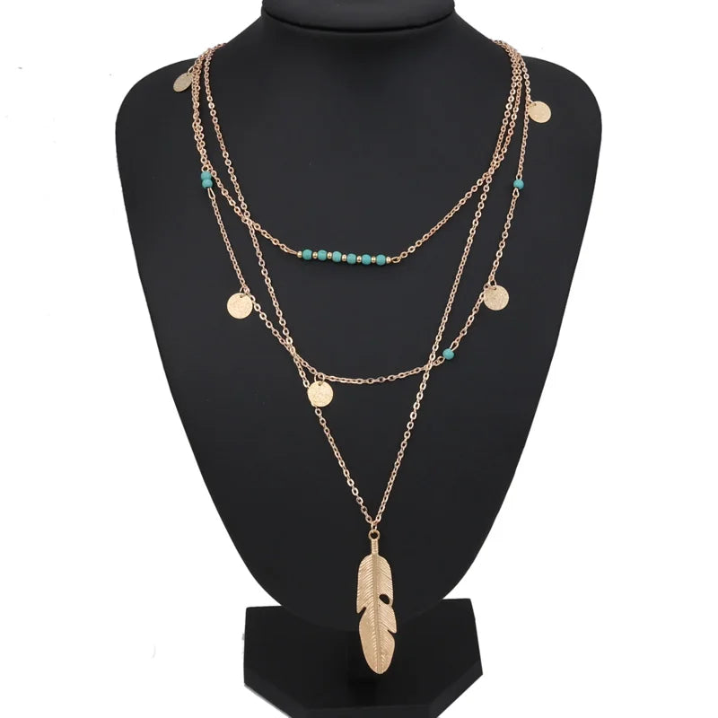 Gold-colored multilayer chain necklace with turquoise beads, coin charms, and a feather pendant.